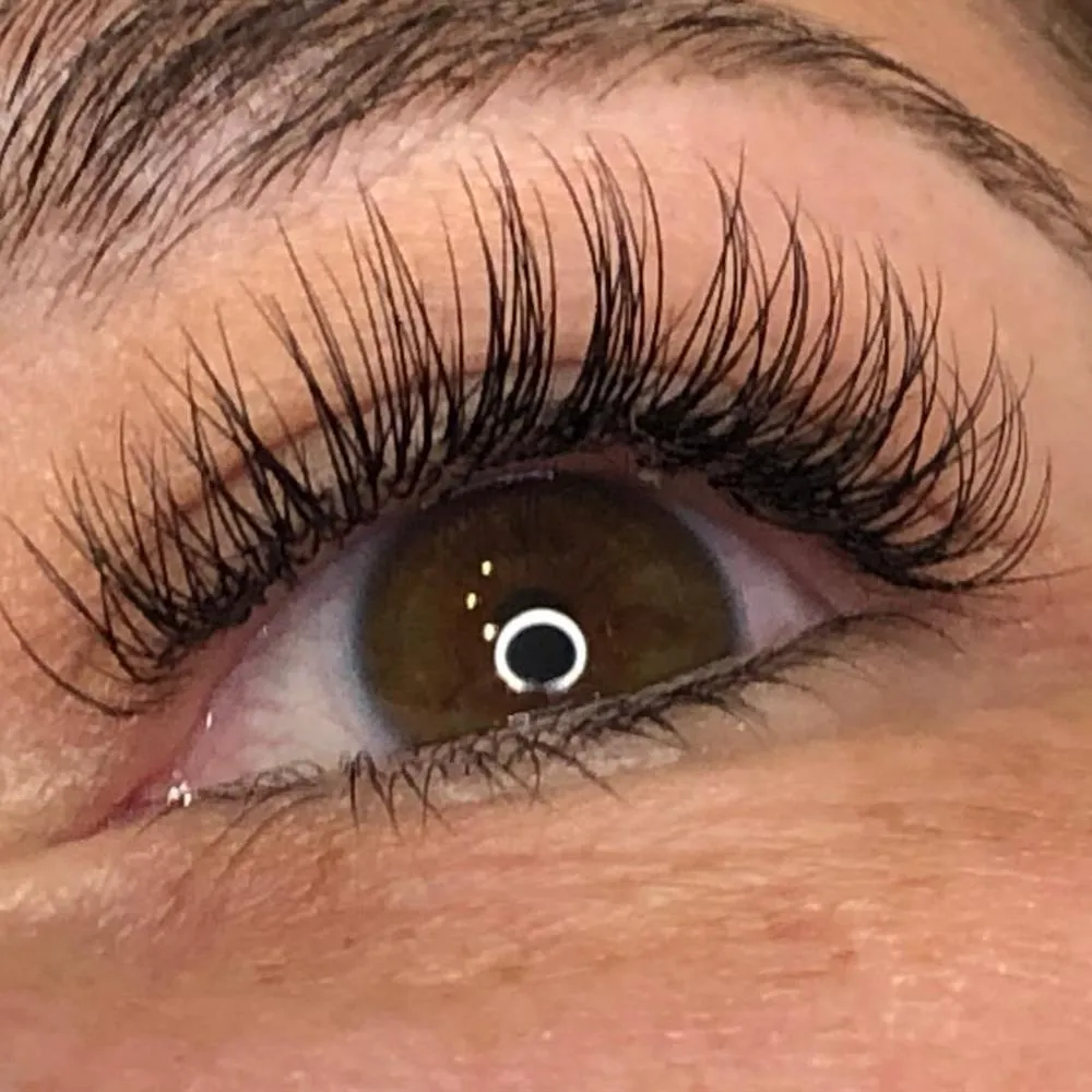 Wimpernverlängerung, Nahaufnahme eines braunen Auges: feine, einzeln gesetzte Wimpern mit weichem Schwung.