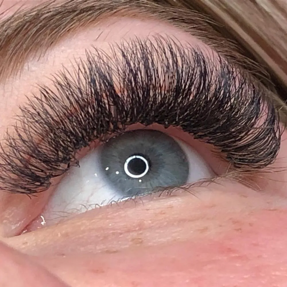 Wimpernverlängerung in kräftigem Volumen: dicht gesetzte Fächer über einem blauen Auge.